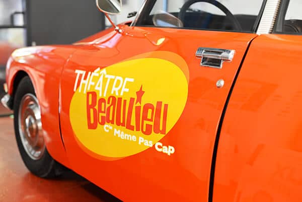 Voiture vintage orange avec logo du Théâtre Beaulieu sur la portière